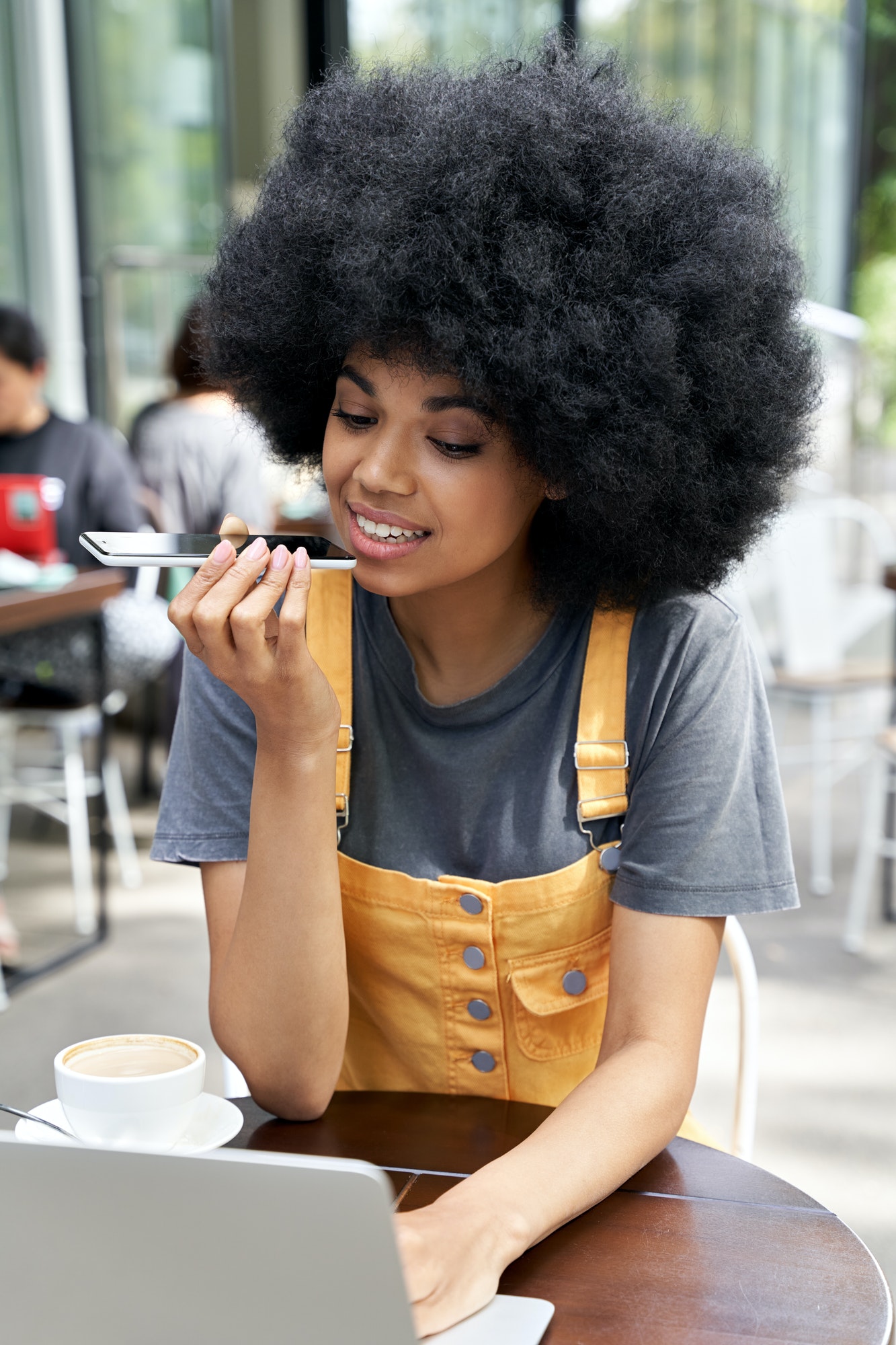 African woman using mobile voice recognition assistant sitting in outdoor cafe.