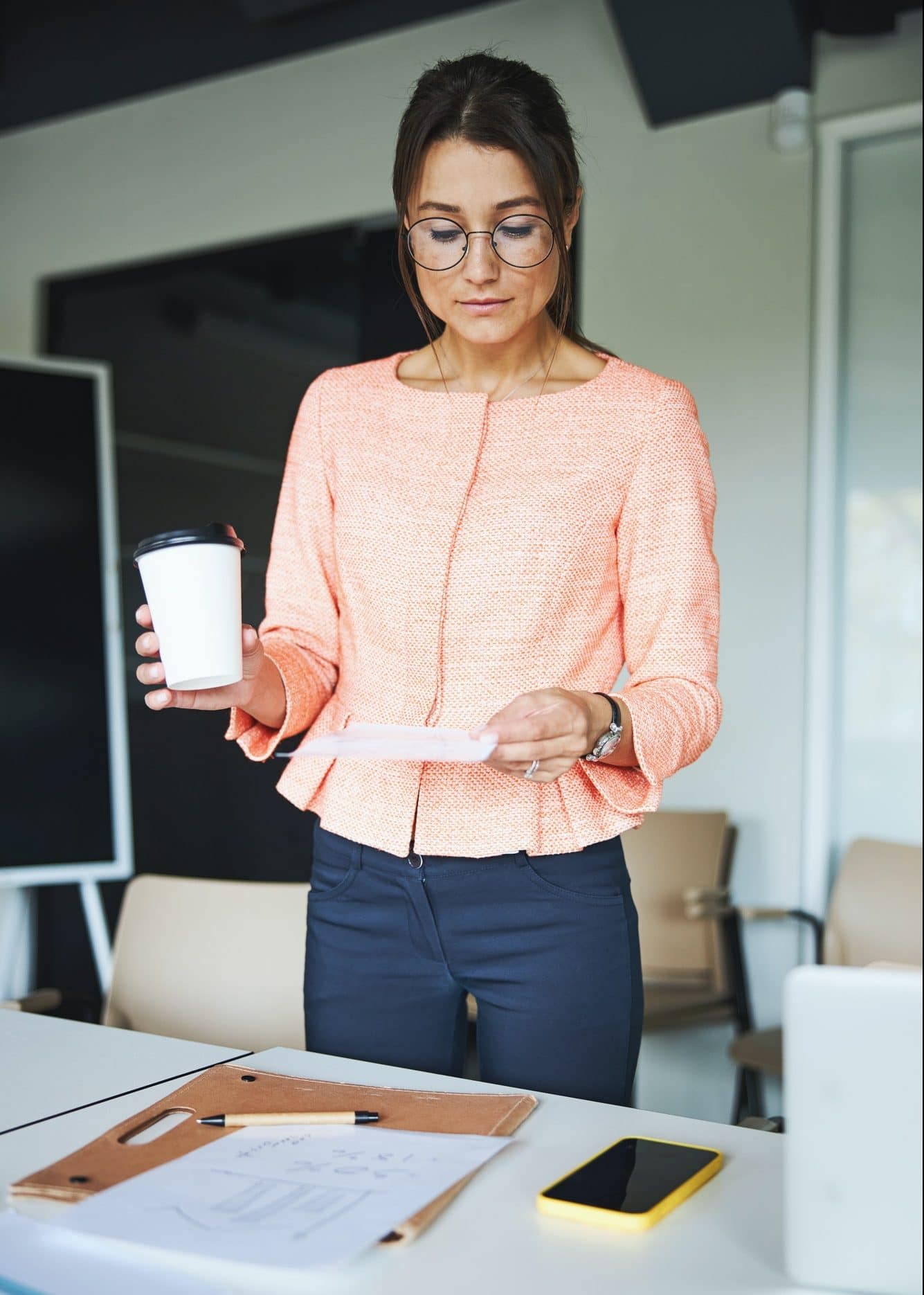 Young Caucasian focused female assistant standing near the work desk and reading report in the