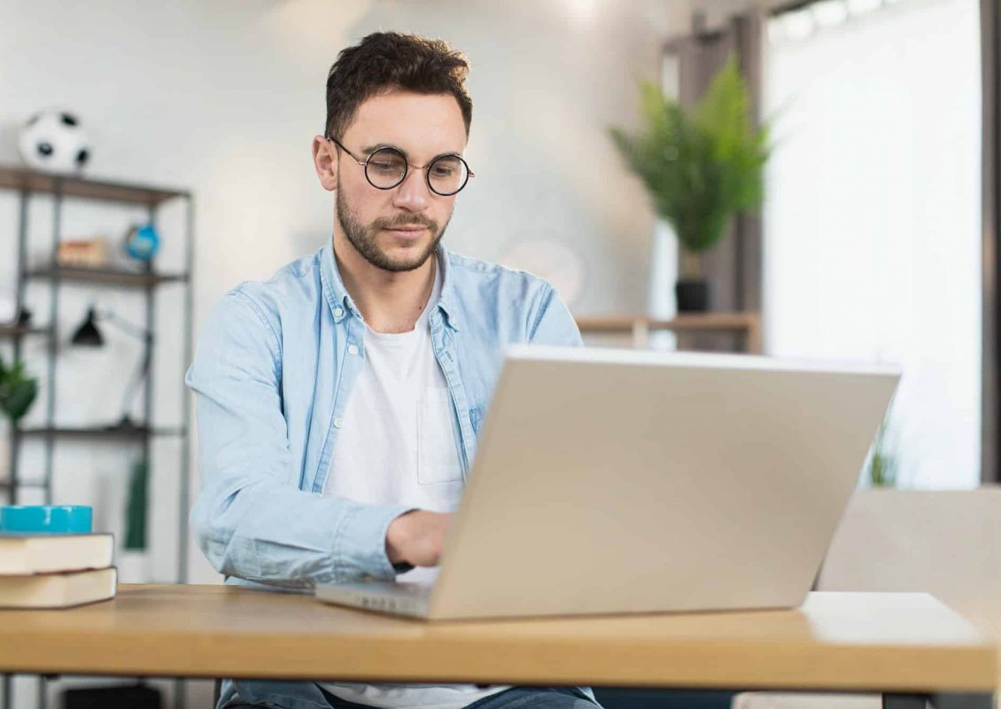 Man in eyewear sitting at desk and working on laptop